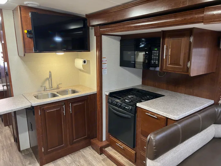 RV rental interior shows a well-equipped kitchen: double sink, microwave, gas range, mounted TV, and wood cabinets.. Other Other 2018