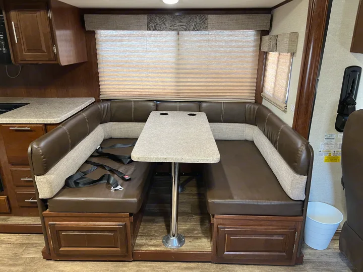 Spacious RV rental dinette featuring a U-shaped booth, sturdy table, kitchen counter, and window with blinds.. Other Other 2018