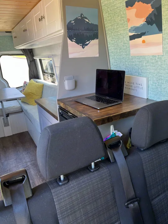 View inside an RV rental, showing a well-appointed workspace with a laptop, bench seating, and overhead storage for travel.. Mercedes-Benz Sprinter 2013
