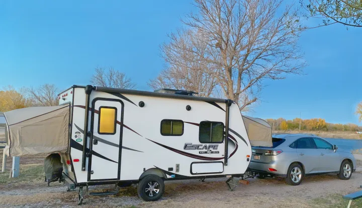 White hybrid travel trailer RV rental with pop-out bunks parked lakeside with an SUV, ready for a camping adventure.. K-Z Manufacturing Escape 2017