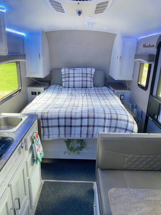 Cozy RV rental interior featuring a plaid bed, kitchen area, and dinette. Blue LED lights add ambiance.. Forest River Rockwood 2020