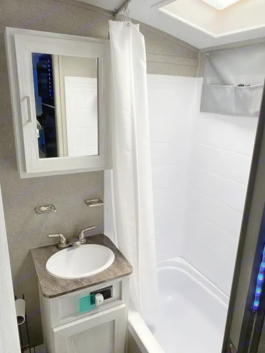 Compact RV rental bathroom features a sink vanity, mirrored cabinet, and a bright tub/shower area.. Forest River Rockwood 2020