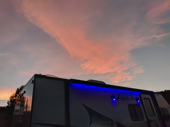 An RV rental at dusk, with glowing blue lights under a sky painted with vibrant pink and orange sunset clouds.. Coachmen Apex 2018