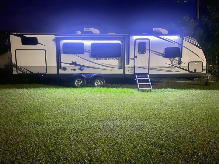 This glowing White Hawk RV rental lights up the night. A modern travel trailer parked on lush grass.. Jayco White Hawk 2022