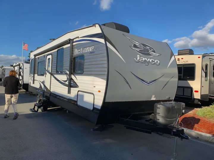 A sleek grey and white Jayco Octane SL travel trailer is displayed outdoors, with a person walking nearby.. Jayco Octane 2019