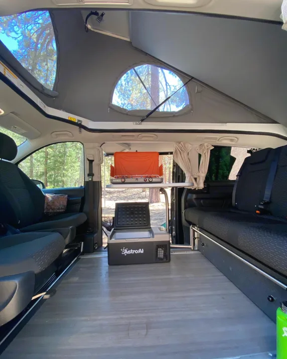 Pop-top RV rental interior: A compact kitchen setup with stove and fridge, plus convertible seating, ideal for nature trips.. Mercedes-Benz Metris Weekender 2021