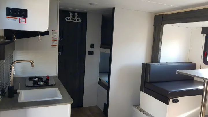 Interior of an RV rental showing a kitchenette (sink, stove), dining booth, and bunk beds.. Keystone RV Hideout 2022