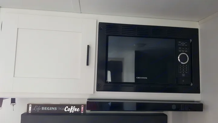 Inside an RV rental, this compact kitchen includes a Greystone microwave, white cabinets, and a coffee-themed sign.. Keystone RV Hideout 2022