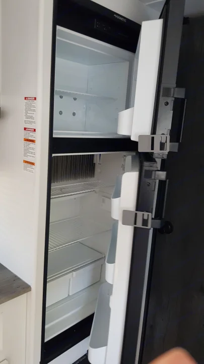 Inside an empty Dometic RV refrigerator, a vital appliance for any RV rental. Features freezer, fridge, and safety labels.. Keystone RV Hideout 2022