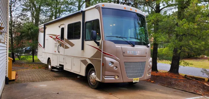 Beige Winnebago Class A RV rental on a paved driveway surrounded by trees, steps extended for next adventure.. Winnebago Vista 2016