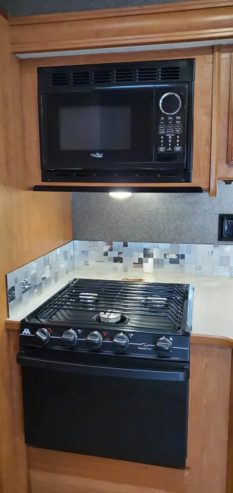 RV rental kitchen: Black microwave above a gas stove/oven, with light wood cabinets and a stylish tile backsplash.. Winnebago Vista 2016