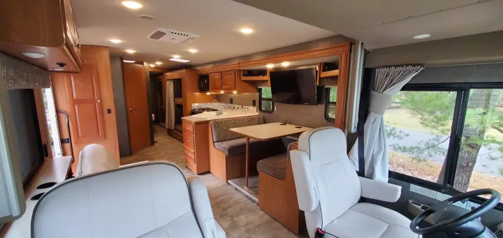Spacious RV rental interior featuring a kitchen, dining booth, comfy captain chairs, and rear bunk beds.. Winnebago Vista 2016