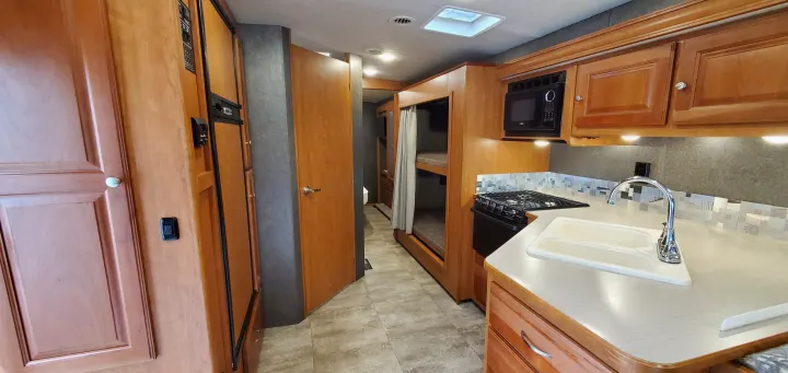 RV rental interior: A full kitchen with stove, sink, microwave, plus bunk beds and a hallway leading to the rear.. Winnebago Vista 2016