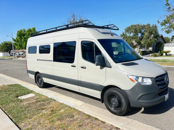 Modern light-colored Mercedes Sprinter van, equipped with a roof rack, available for RV rental.. Mercedes Sprinter 2021
