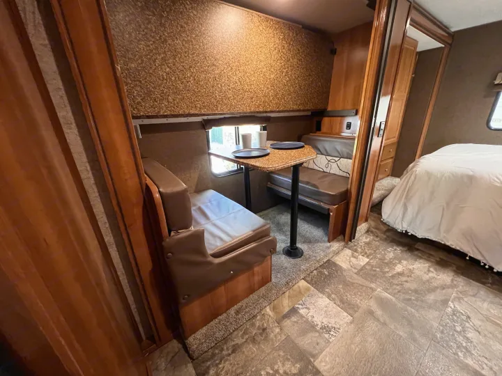 Inside this RV rental: a compact dinette with benches and table, transitioning to a bright bedroom area. Mixed flooring and wood accents.. Other Other 2018