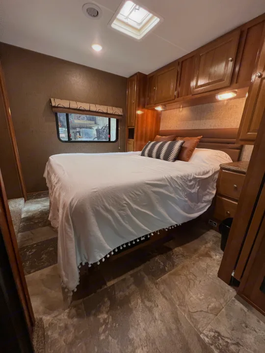 RV rental bedroom: a comfy bed with white sheets, wood cabinets, and bright lights overhead for a restful stay.. Other Other 2018