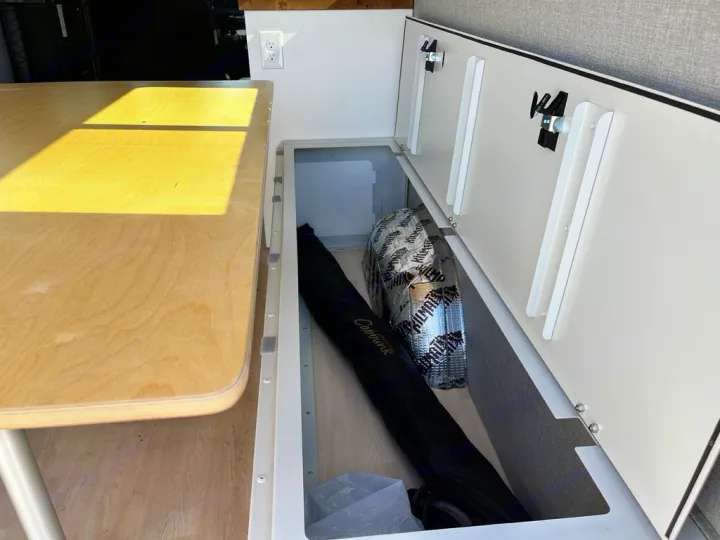 RV rental interior: practical under-bench storage with Kilmat insulation, a black bag, and clean white cabinets.. Mercedes Sprinter 2021