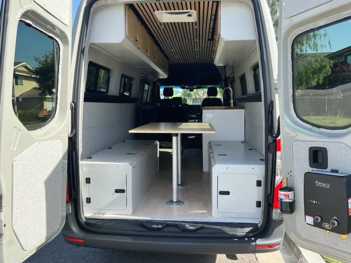 RV rental: Camper van interior reveals a versatile table, long storage benches, overhead cabinets, and rear water heater unit.. Mercedes Sprinter 2021