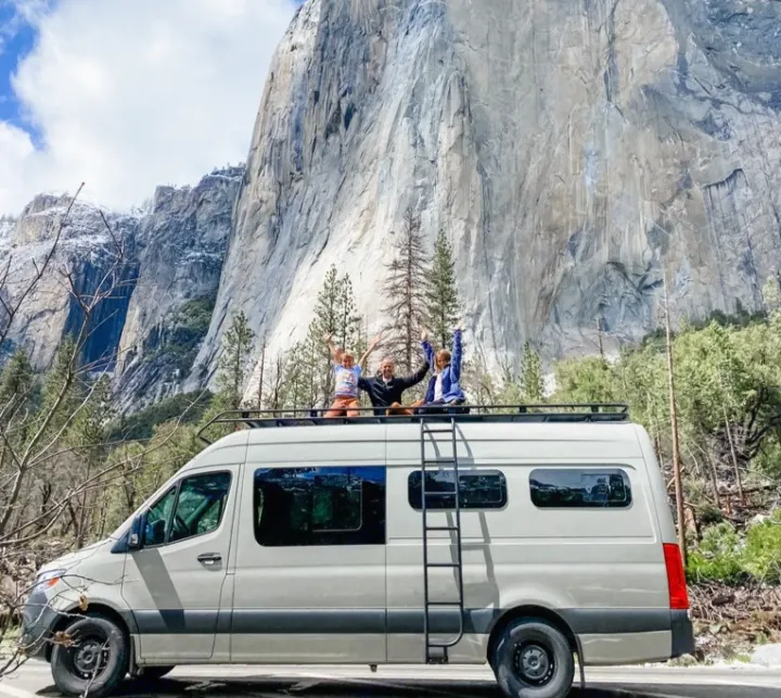 Joyful family on an RV rental van's roof, arms raised, against Yosemite's majestic El Capitan. Epic van life!. Mercedes Sprinter 2021