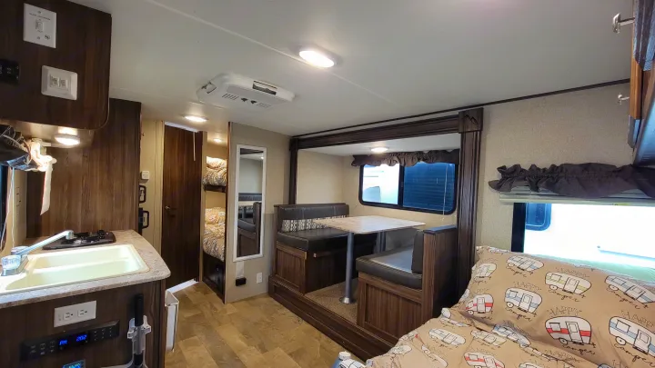 RV rental interior showcasing a practical kitchen, cozy dinette, bunk beds, and a main sleeping area with fun camper bedding.. Coachmen Apex 2018