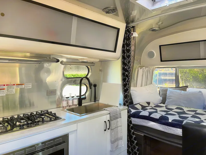 Modern Airstream RV rental interior, showcasing a sleek kitchen with stove, sink, and a comfortable bed area.. Airstream Caravel 2022