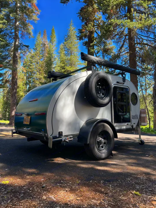 Teardrop RV rental parked in a sunny forest setting, ideal for outdoor adventures and camping trips.. Teardrops Northwest Trek 2022