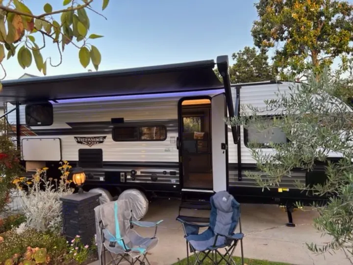 Perfect RV rental setup! This travel trailer features an extended awning with ambient blue lights, camping chairs, and an inviting outdoor space.. Forest River Wildwood X-Lite 2022