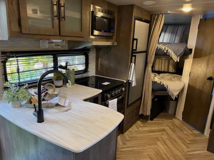RV rental interior featuring a modern kitchen area, large fridge, and comfortable bunk beds. Perfect for family trips.. Forest River Wildwood X-Lite 2022