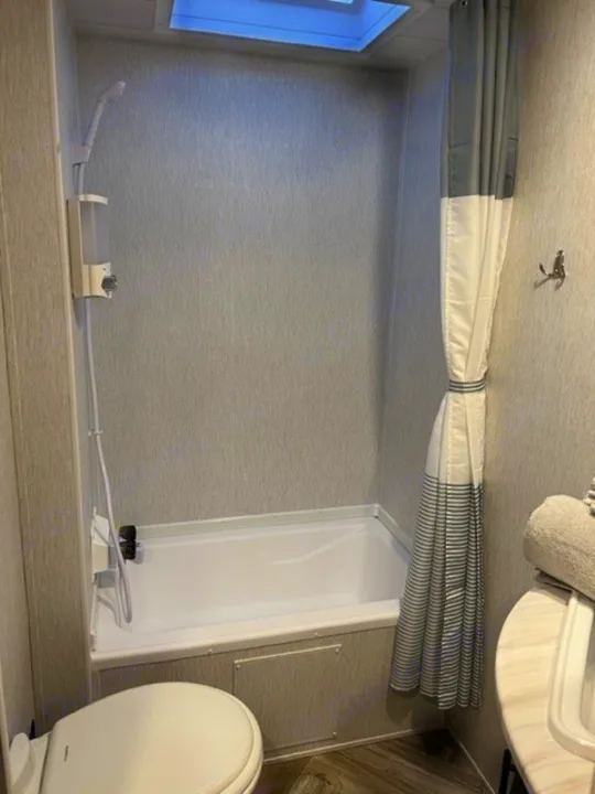 Inside an RV rental: a modern bathroom with a tub/shower combo, toilet, vanity, and skylight. Enjoy comfort on the road.. Forest River Wildwood X-Lite 2022
