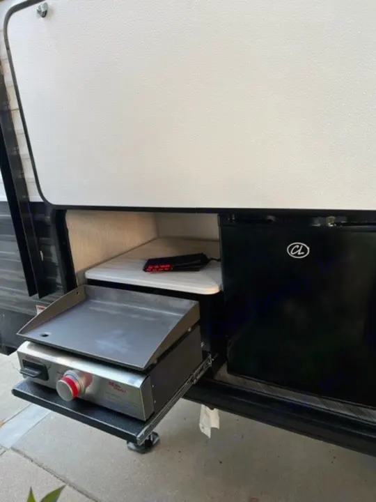 RV rental outdoor kitchen setup with a pull-out griddle and compact refrigerator. Ideal for convenient camping meals.. Forest River Wildwood X-Lite 2022