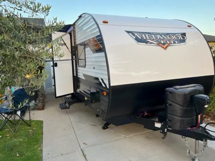 This white and black travel trailer, an RV rental, is parked on a driveway with its door open, ready for adventure.. Forest River Wildwood X-Lite 2022