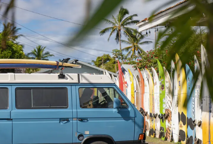 Blue VW camper van with surfboards on top, a perfect RV rental for adventures, parked by a vibrant display of surfboards.. VW Westfalia 1990