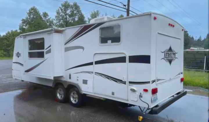 White Aerolite travel trailer with slide-out, perfect for your next rv rental. Shown parked on a wet surface.. Aerolite Aerolite Trailer 2008