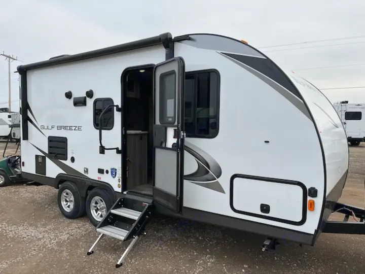 Bright white travel trailer RV rental, labeled 'GULF BREEZE', with its entrance door open and steps extended.. Gulf Stream 21QBS 2022