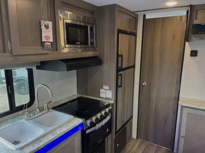 Inside an RV rental: a modern kitchen galley with a dual sink, stove, microwave, refrigerator, and ample storage.. Gulf Stream 21QBS 2022