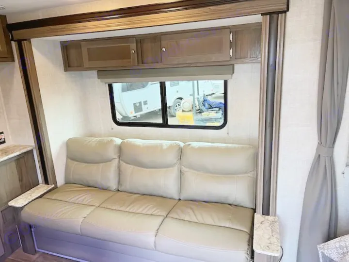 Comfortable RV rental living area featuring a large tan sofa, overhead cabinets, and a window for scenic views.. Gulf Stream 21QBS 2022