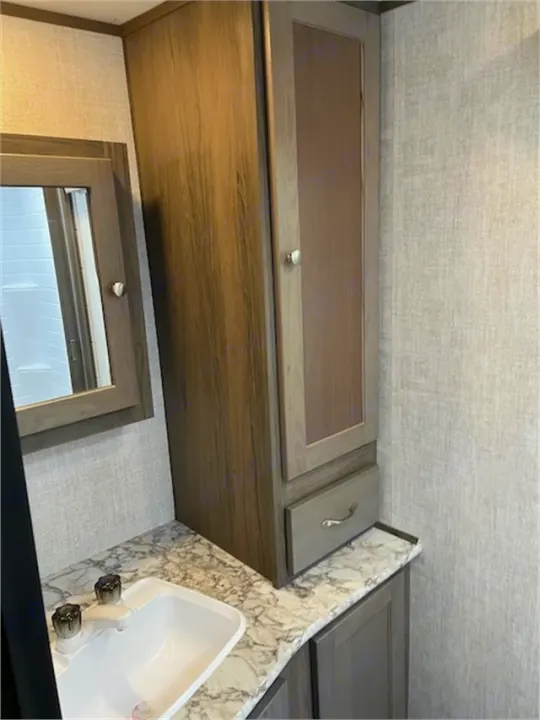 Modern RV rental bathroom with a white sink, marble-look counter, mirror, and tall wood-tone storage cabinet for your convenience.. Gulf Stream 21QBS 2022