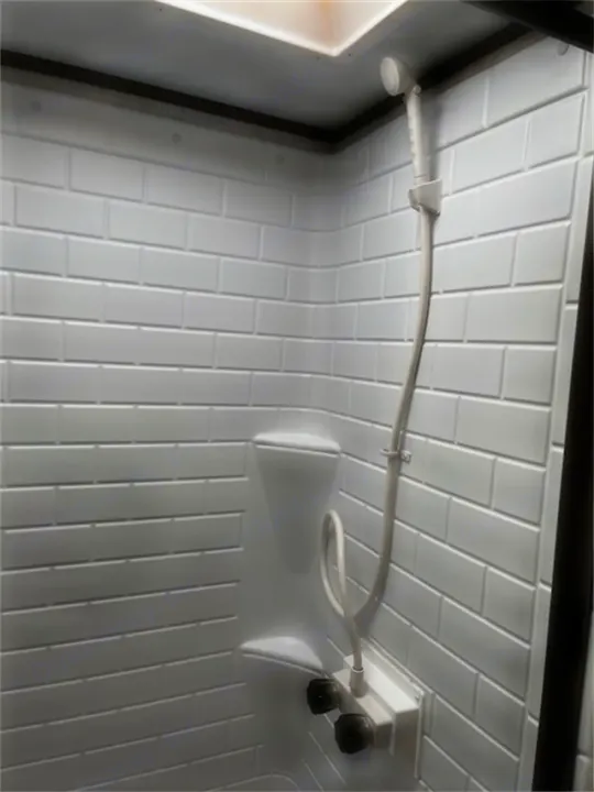 Compact white shower stall in an RV rental, featuring a handheld showerhead, water controls, and a built-in shelf.. Gulf Stream 21QBS 2022