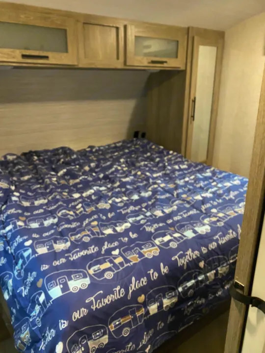 RV rental bedroom: a cozy bed with blue travel-themed bedding (campers, "Together is our favorite place to be" text) and wooden cabinets.. Forest River Salem Hemisphere HL 2021