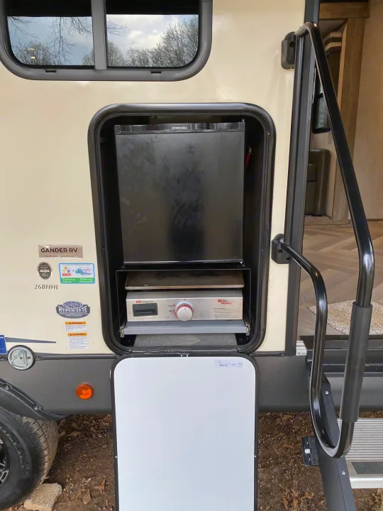 An RV rental's side compartment is open, revealing a pull-out outdoor kitchen with an EverChill fridge and Suburban griddle.. Forest River Salem Hemisphere HL 2021