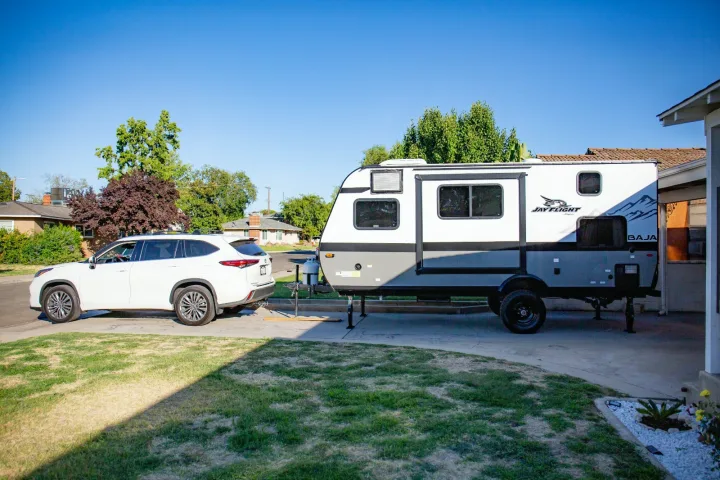 White SUV connected to a Jay Flight Baja travel trailer in a sunny driveway, ready for an RV rental adventure.. Jayco Jay flight slx 7 2022