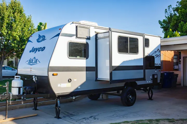 Jayco Baja RV rental: A white and gray travel trailer is parked on a driveway, with its door open, showing windows and leveling jacks.. Jayco Jay flight slx 7 2022