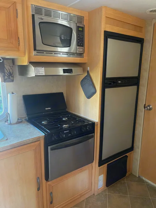 RV rental kitchen: light wood cabinets, stainless microwave, gas stove/oven, and two-door fridge. Compact setup for travel.. Aerolite Aerolite Trailer 2008