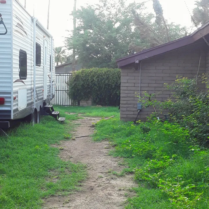 A white RV rental travel trailer is parked on a spacious grassy and dirt lot, adjacent to a small building and trees.. Heartland RVs Trail Runner 2013