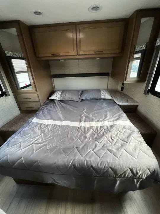 Cozy RV rental bedroom with a large gray bed, overhead cabinets, and side nightstands. Bright interior for your journey.. Coleman Other 2022