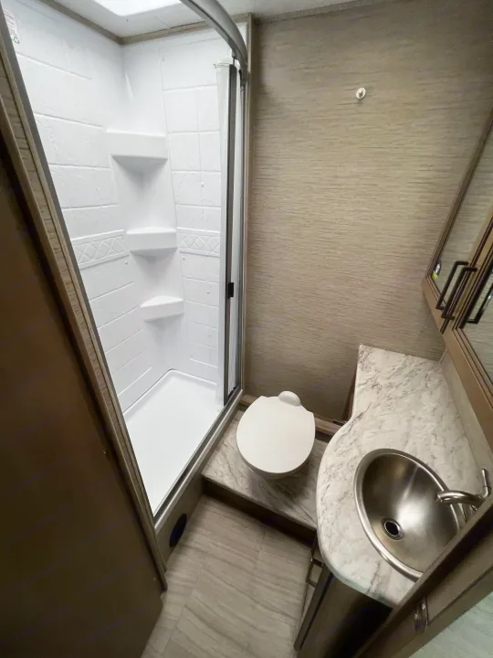 This clean RV rental bathroom features a white shower, toilet, and vanity with a steel sink, designed for compact travel comfort.. Coleman Other 2022
