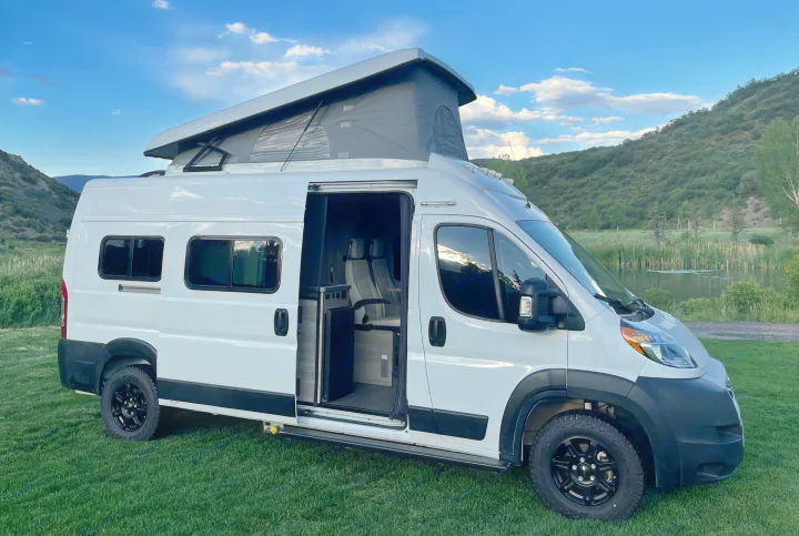 White pop-top camper van parked in a scenic mountain setting, ready for your next rv rental adventure. Interior visible through open door.. Winnebago Solis 2021