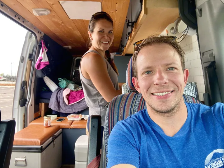 Couple enjoying their cozy RV rental. Van life interior shows bed, kitchen, and custom wood details.. Dodge Sprinter Van 2008