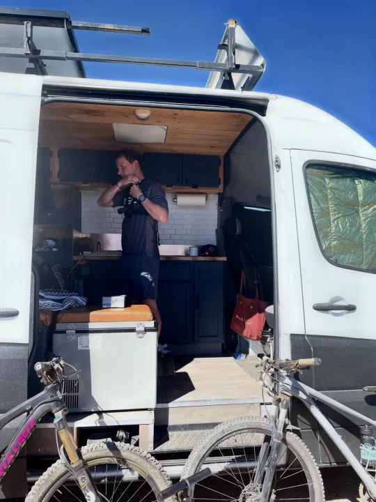 Inside a spacious rv rental van, a man adjusts his gear while mountain bikes await outside for an epic adventure.. Dodge Sprinter Van 2008