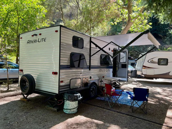 This Ameri-Lite travel trailer is ready for your RV rental adventure, parked in a shady campground with an awning and outdoor setup.. Gulf Stream Amerilite 2022